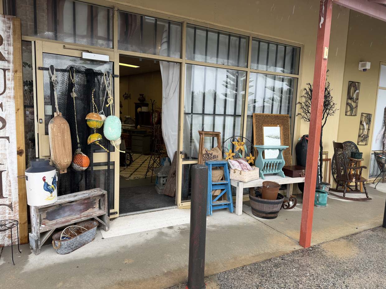 The shopfront: a painted RUSTIC sign, fishing buoys hung on the door, a rooster milk churn on an old bench.