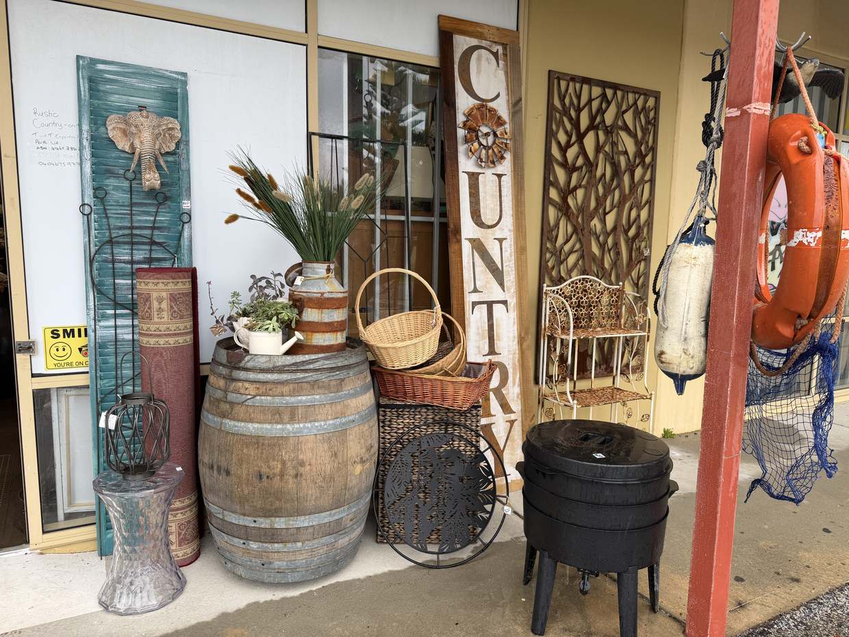 Out the front under the verandah: a wine barrel, baskets, a milk churn, a COUNTRY sign and a cast-iron pot.