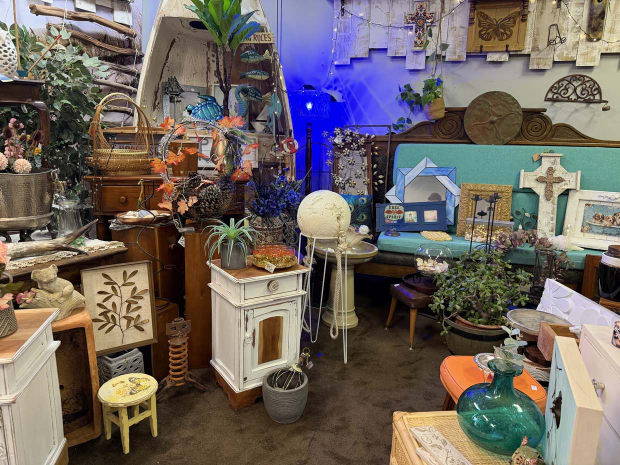 A teal bench seat with crosses, mirrors and framed pictures, beside an upended wooden dinghy.