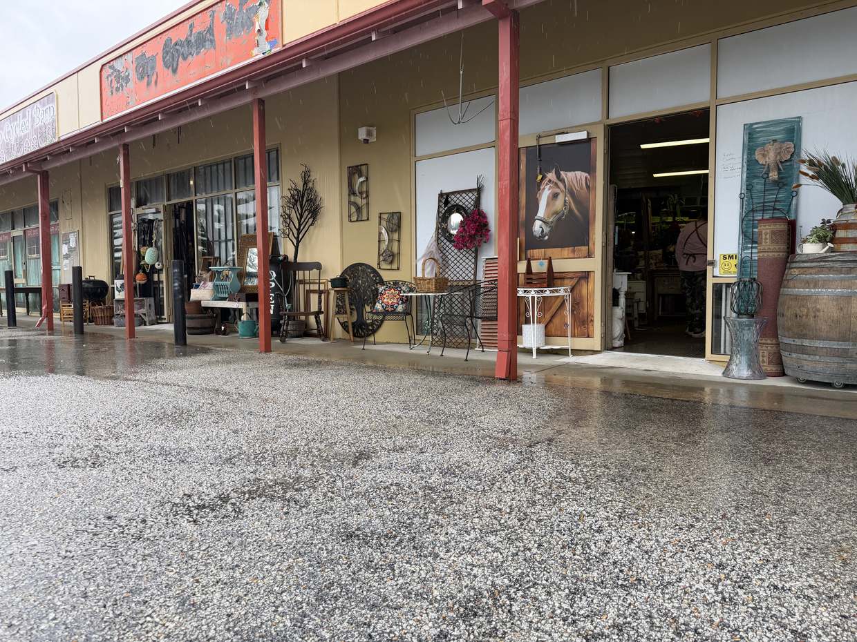 The row of shopfronts under a red verandah on a rainy day, with furniture and mirrors set out along the footpath.