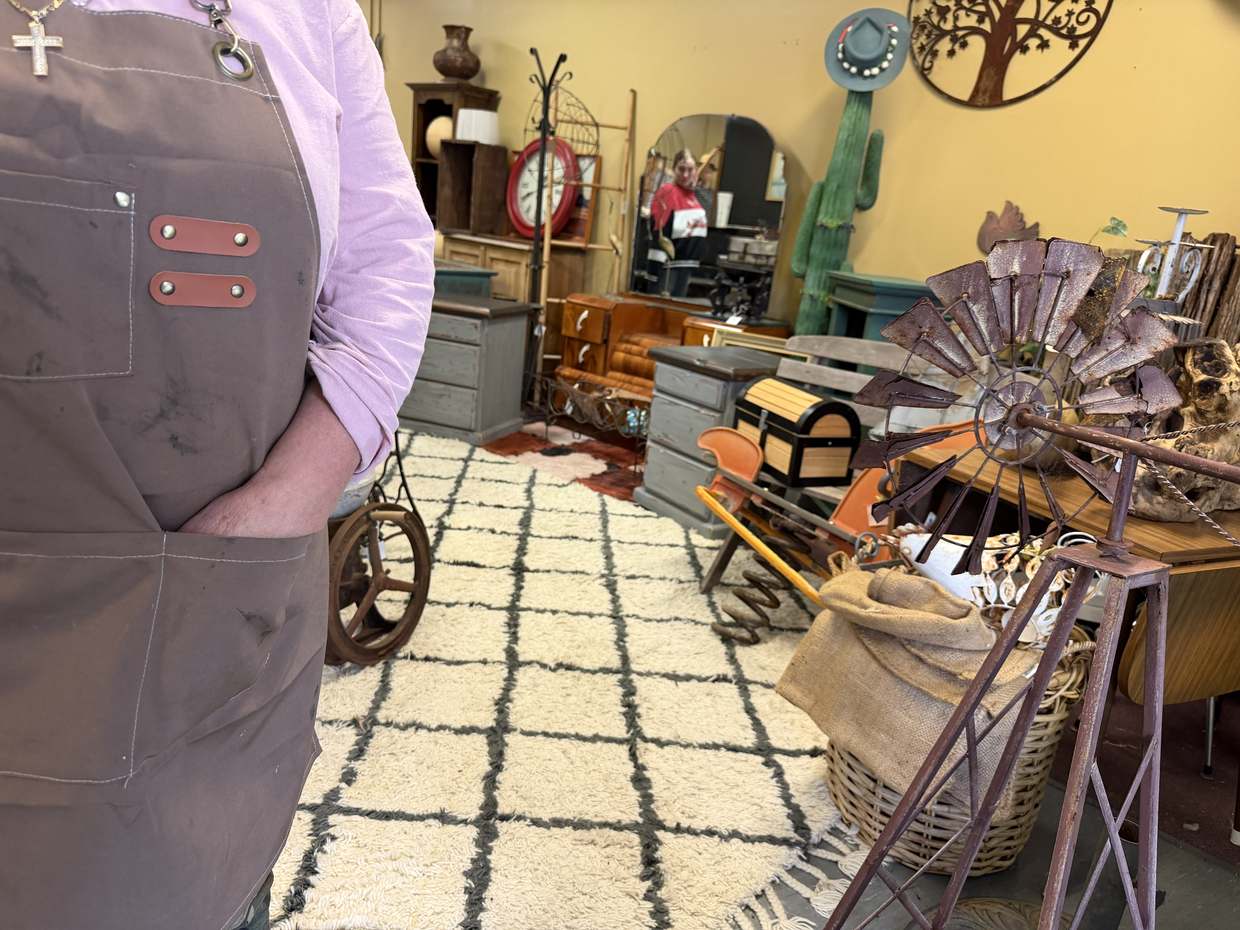Inside the shop, looking across a cream and charcoal rug to painted drawers, a red wall clock and a tall green cactus.
