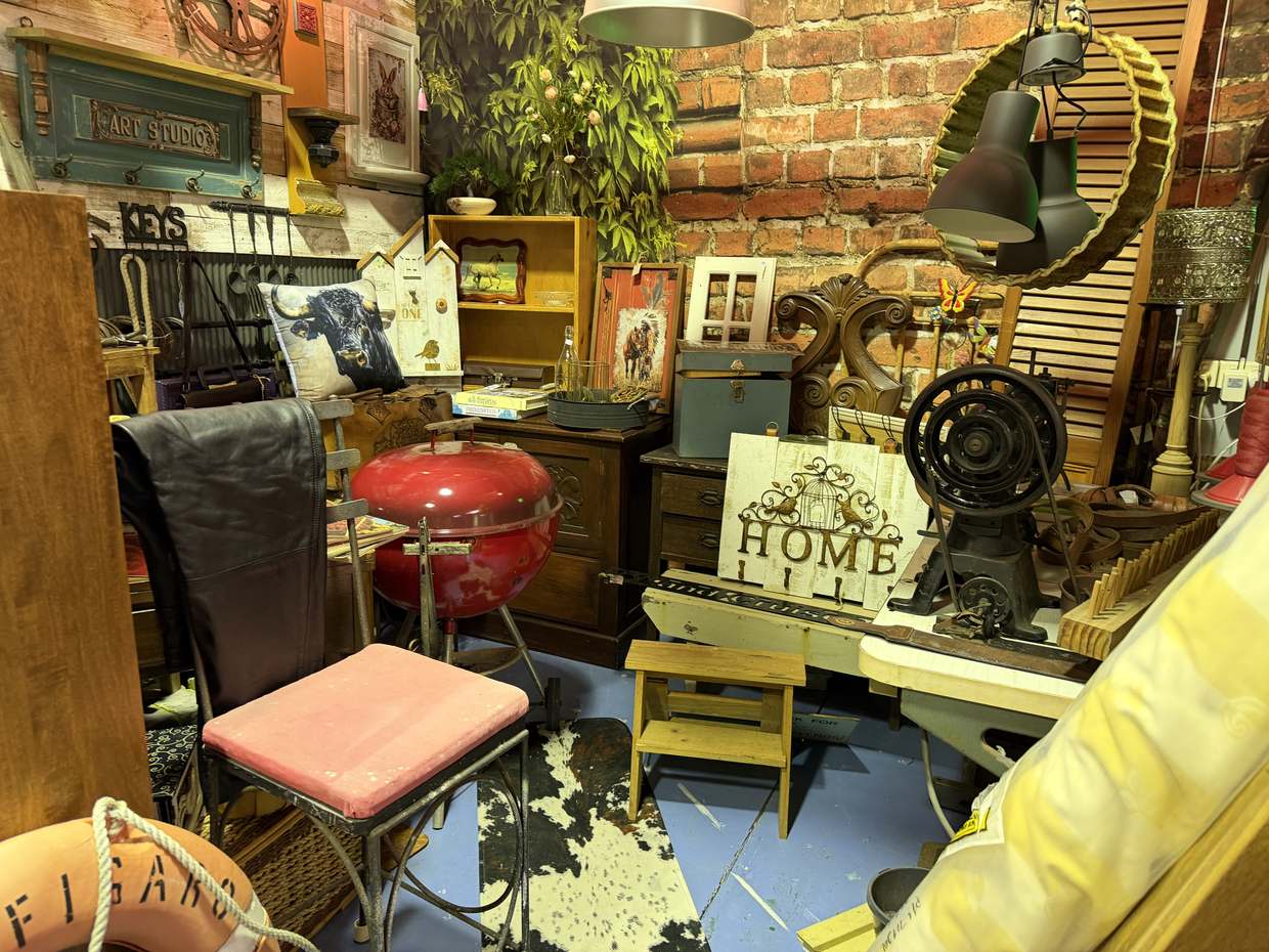A brick wall corner with an ART STUDIO board, a cast-iron sewing machine base, a red kettle barbecue and a HOME sign.