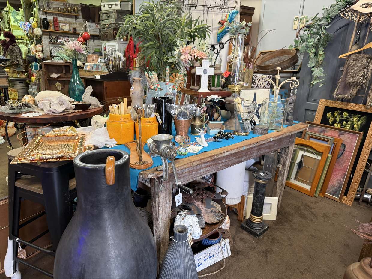 A timber table with a bright blue runner holding orange crockery jars, brass, glassware and a hand mincer.