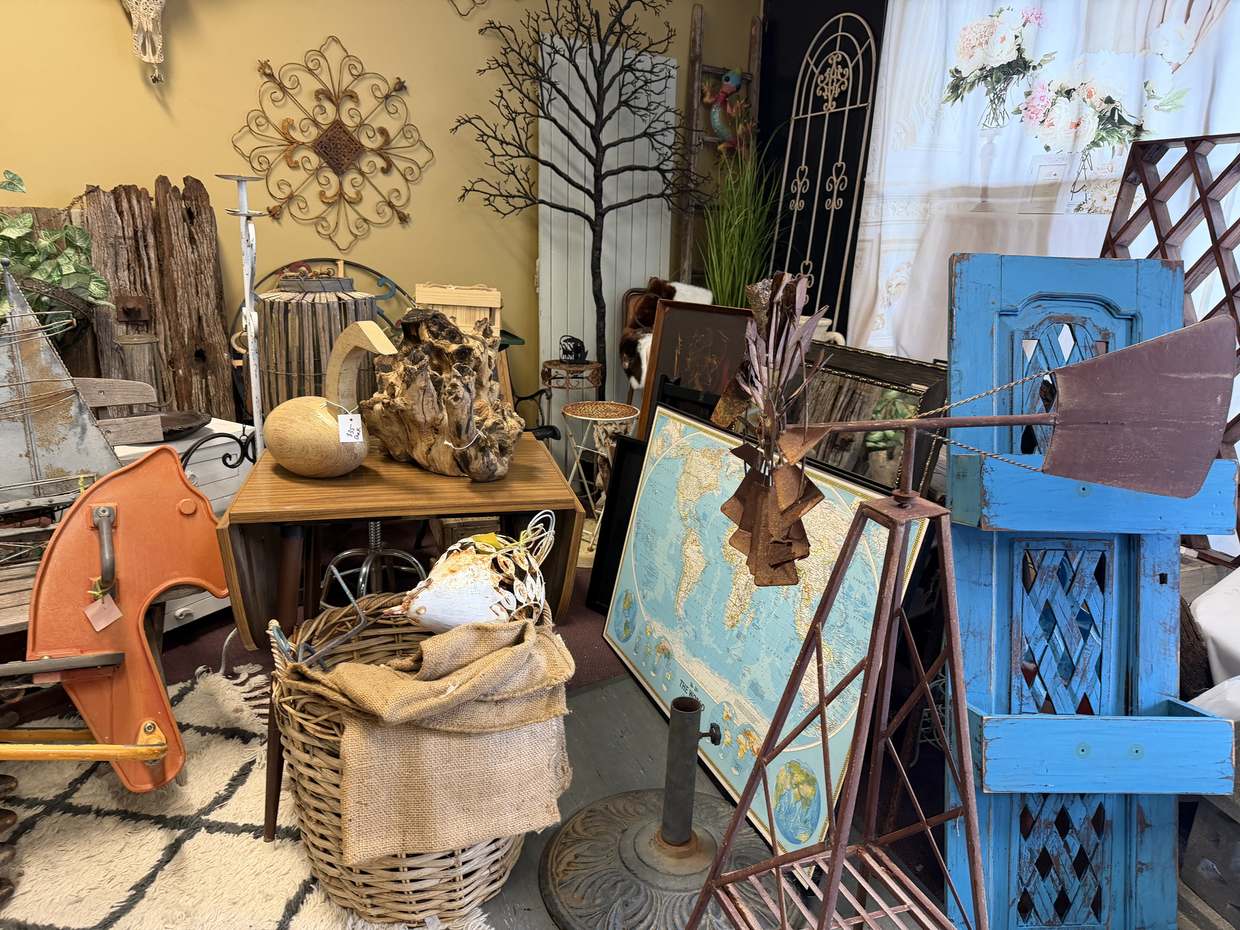 A rusted windmill head in front of a framed world map, beside a bright blue shutter door and an orange rocking horse.